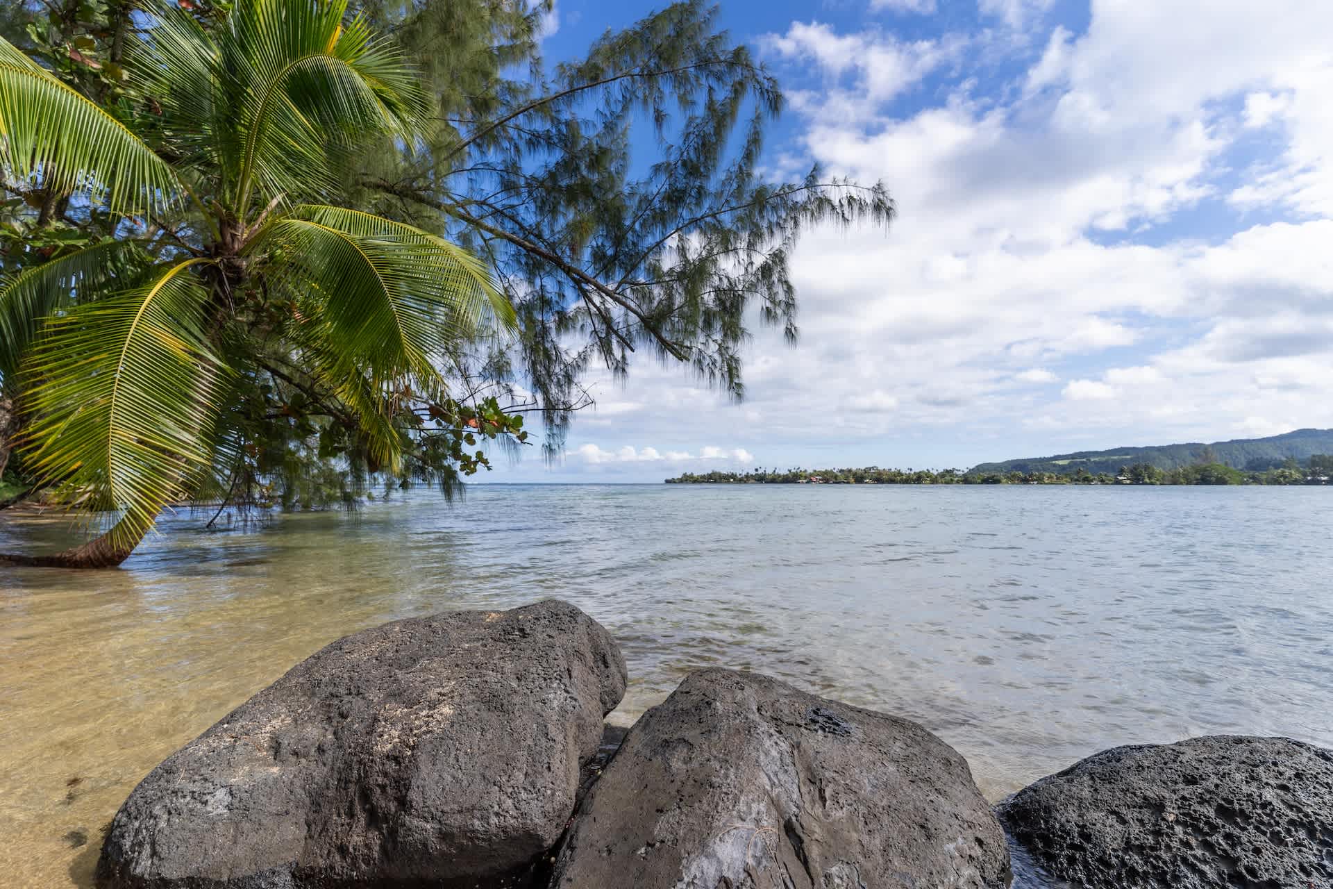 Schwarze Lavafelsen am Lagunenufer, gegenüber die Berge von Tahiti Nui